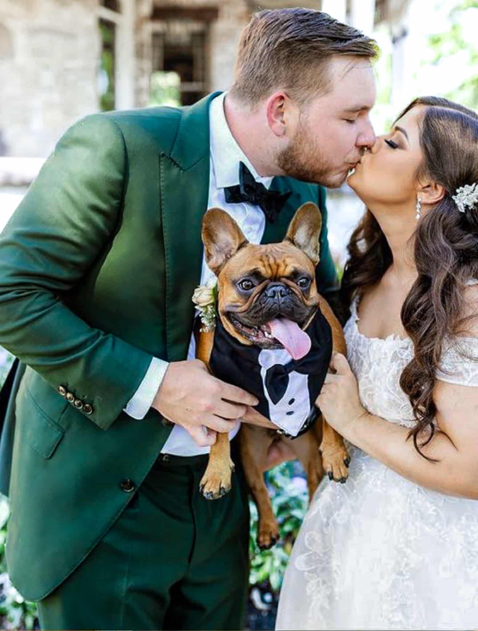 Bride and groom kissing. Groom wearing dark green bespoke suit with white shirt and black bowtie. Fabric by Scabal. Bride in low cut wedding dress.