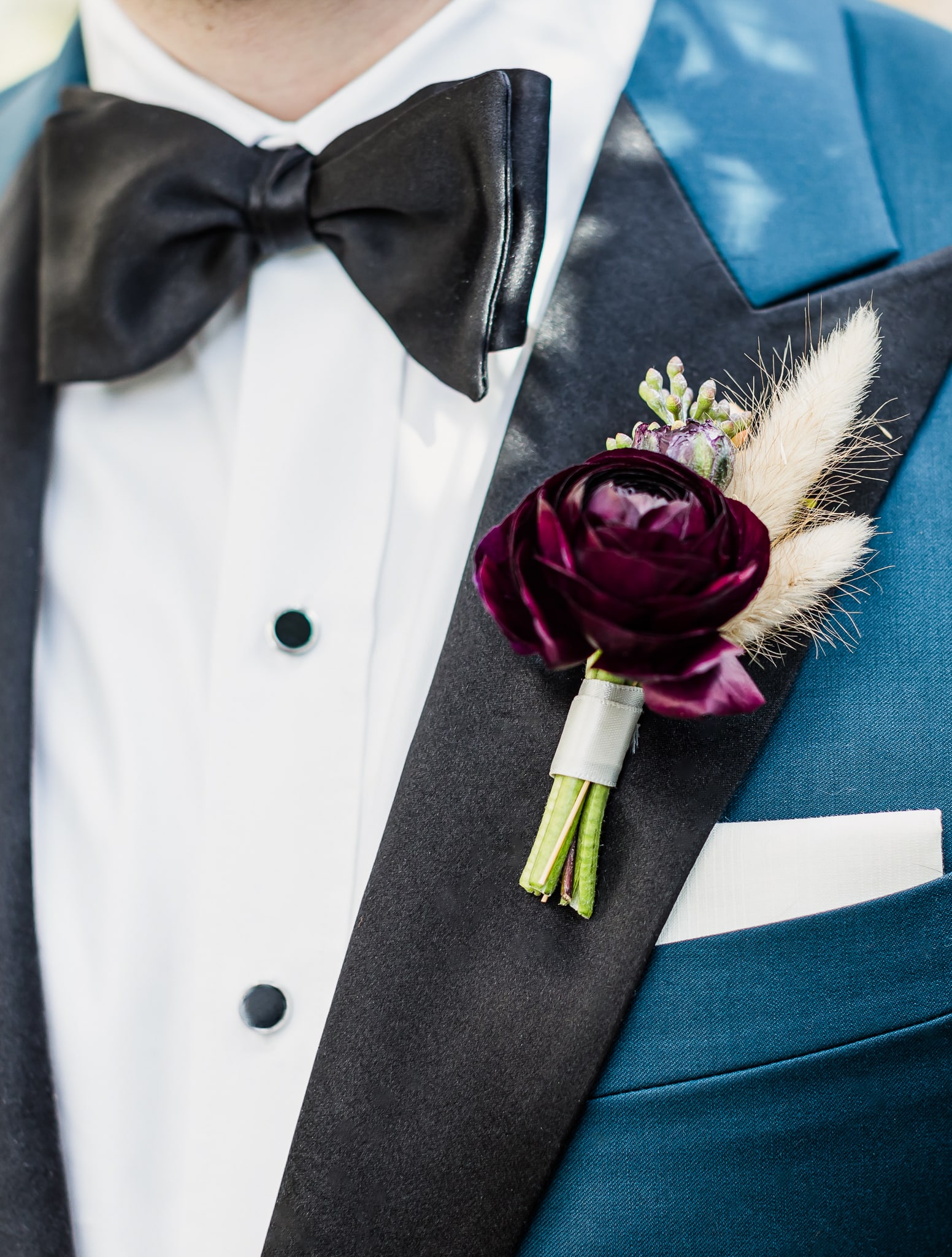 Extreme closeup of grooms wedding tuxedo. French blue solid bespoke tuxedo with black satin, white shirt and black bowtie.