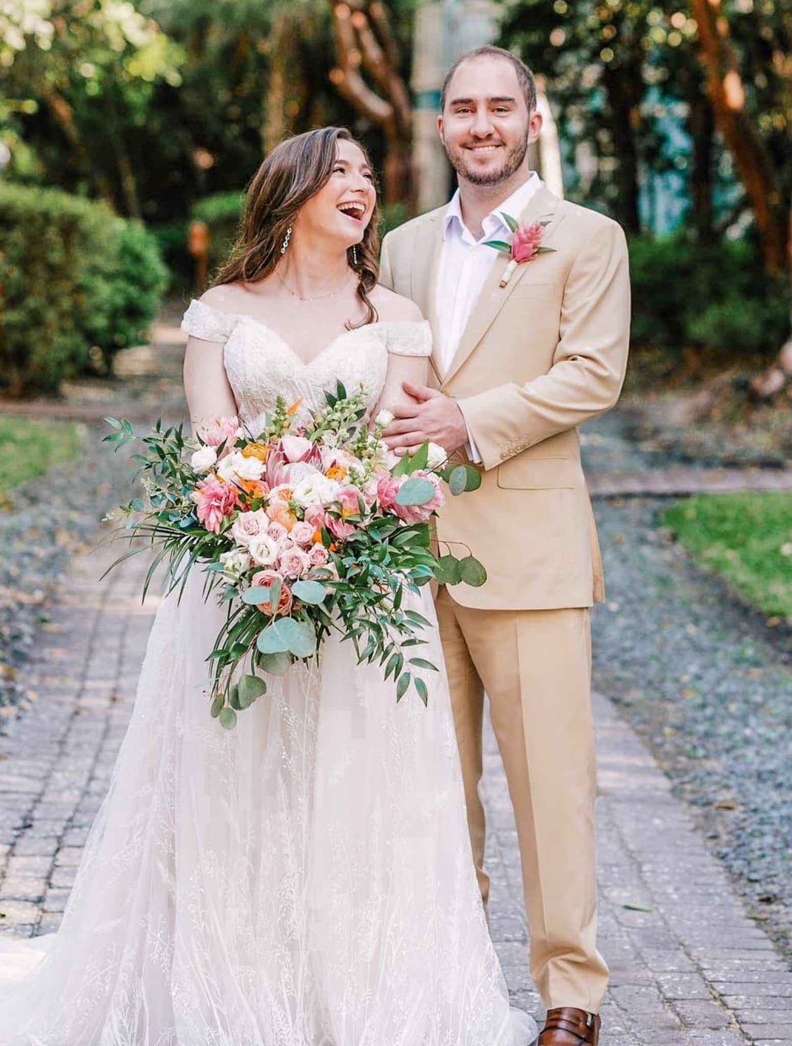 Bride and groom outdoors. Groom wearing Loro Piana linen off-white custom suit with open collared off white shirt. Bride in long wedding gown.