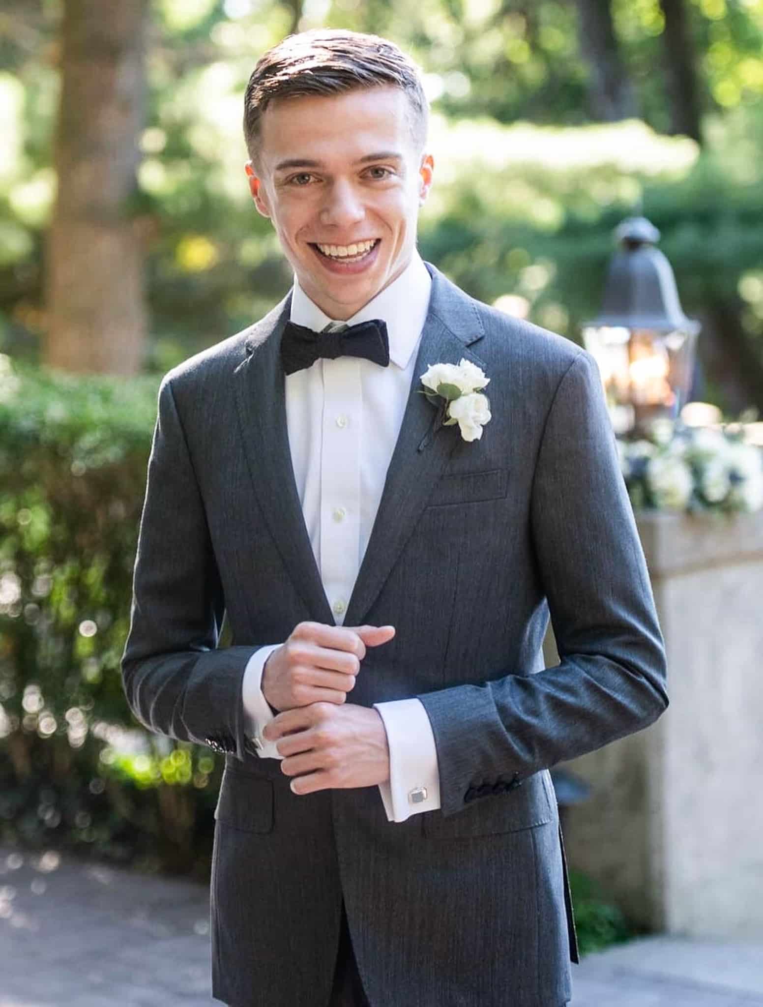 Groom outdoors wearing his custom wedding tuxedo is solid black. White shirt and black skinny bowtie. Tuxedo fabric by Dormeuil.