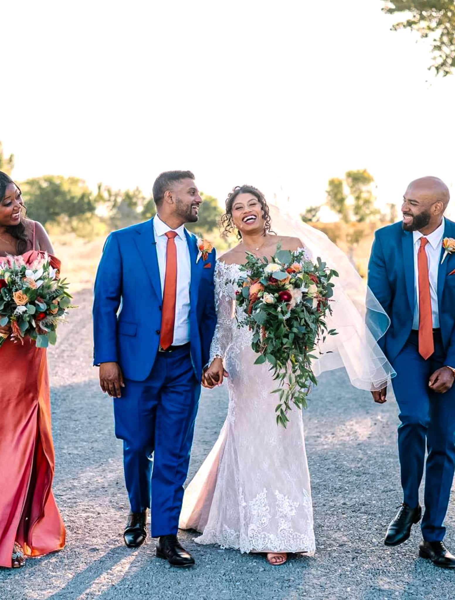 Bride and groom outdoors with mother and father. Groom wearing bespoke wedding suit in bright blue color with white shirt and solid orange skinny long tie. Bride in classic off the shoulder wedding gown.