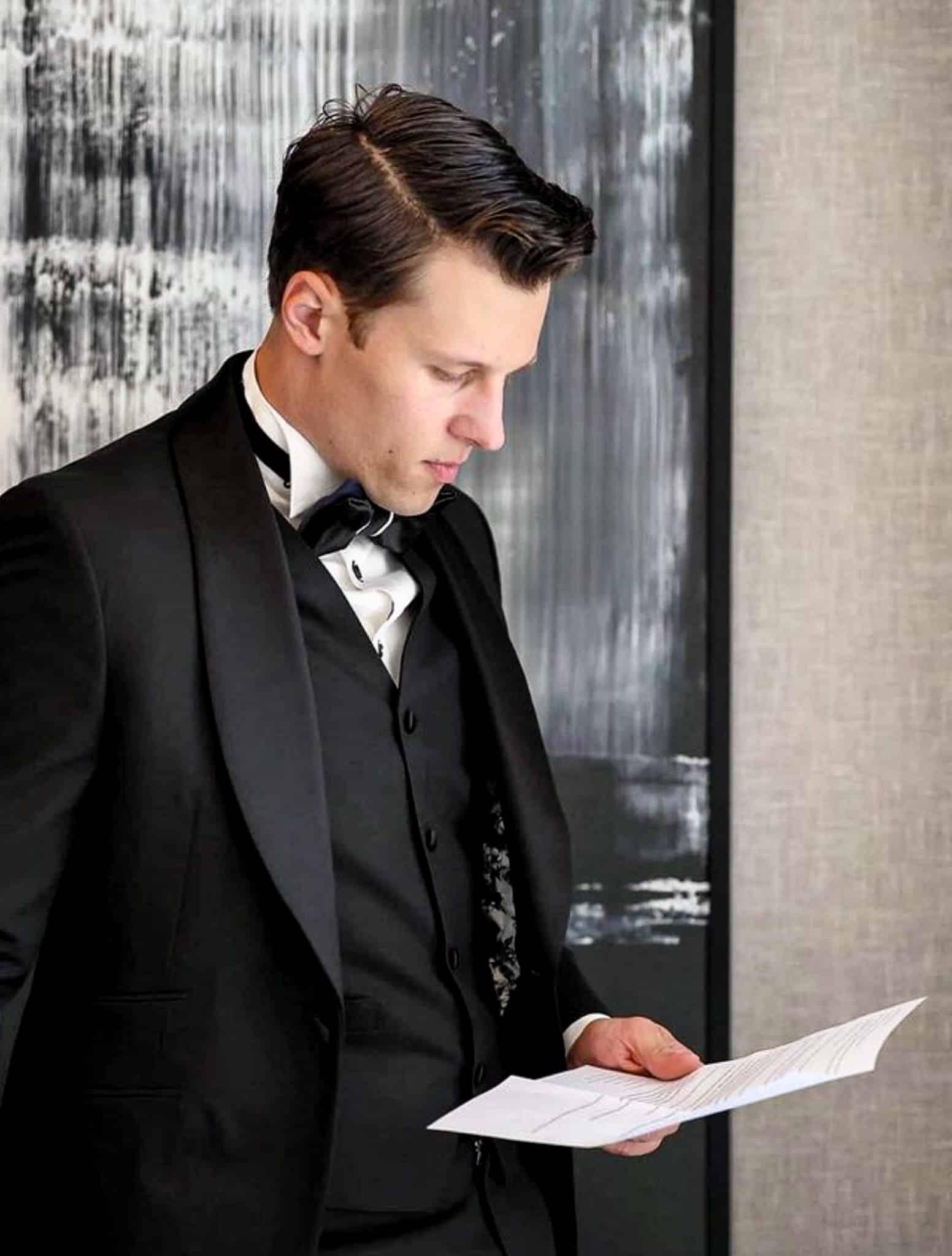 Groom reading speech wearing black tuxedo tails with black vest. Fabric by Ermenegildo Zegna.
