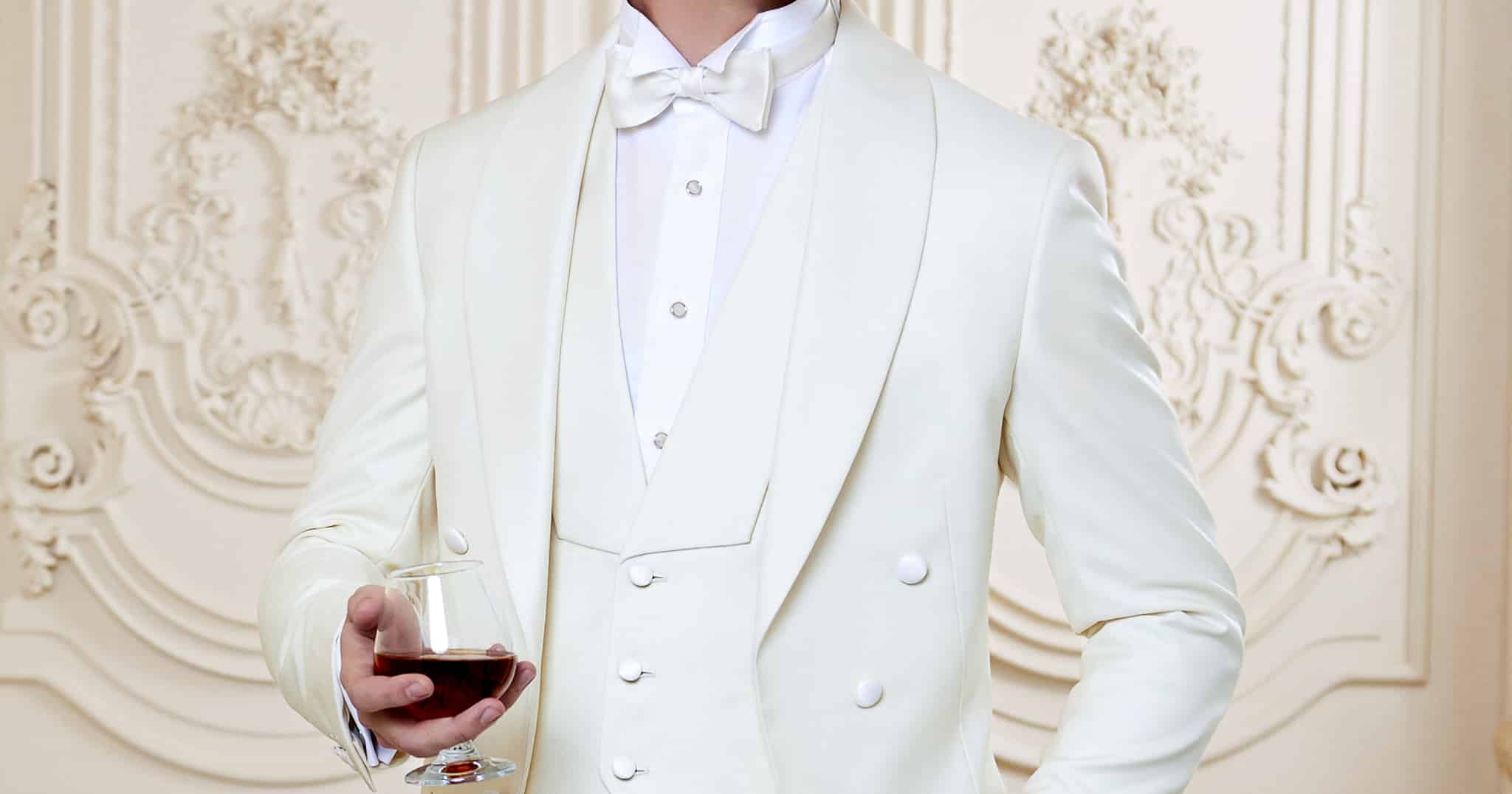 Groom wearing white tuxedo tails with matching white vest, both with shawl lapels.
