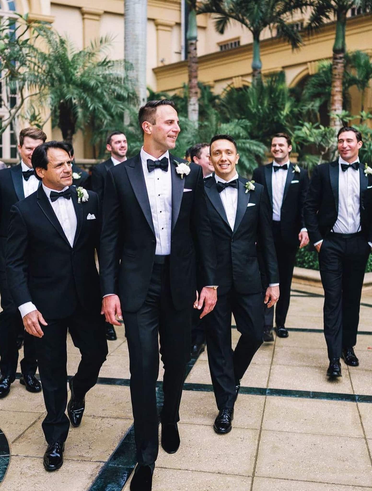 Seven groomsmen waling behind groom-all wearing classic black wedding tuxedos.