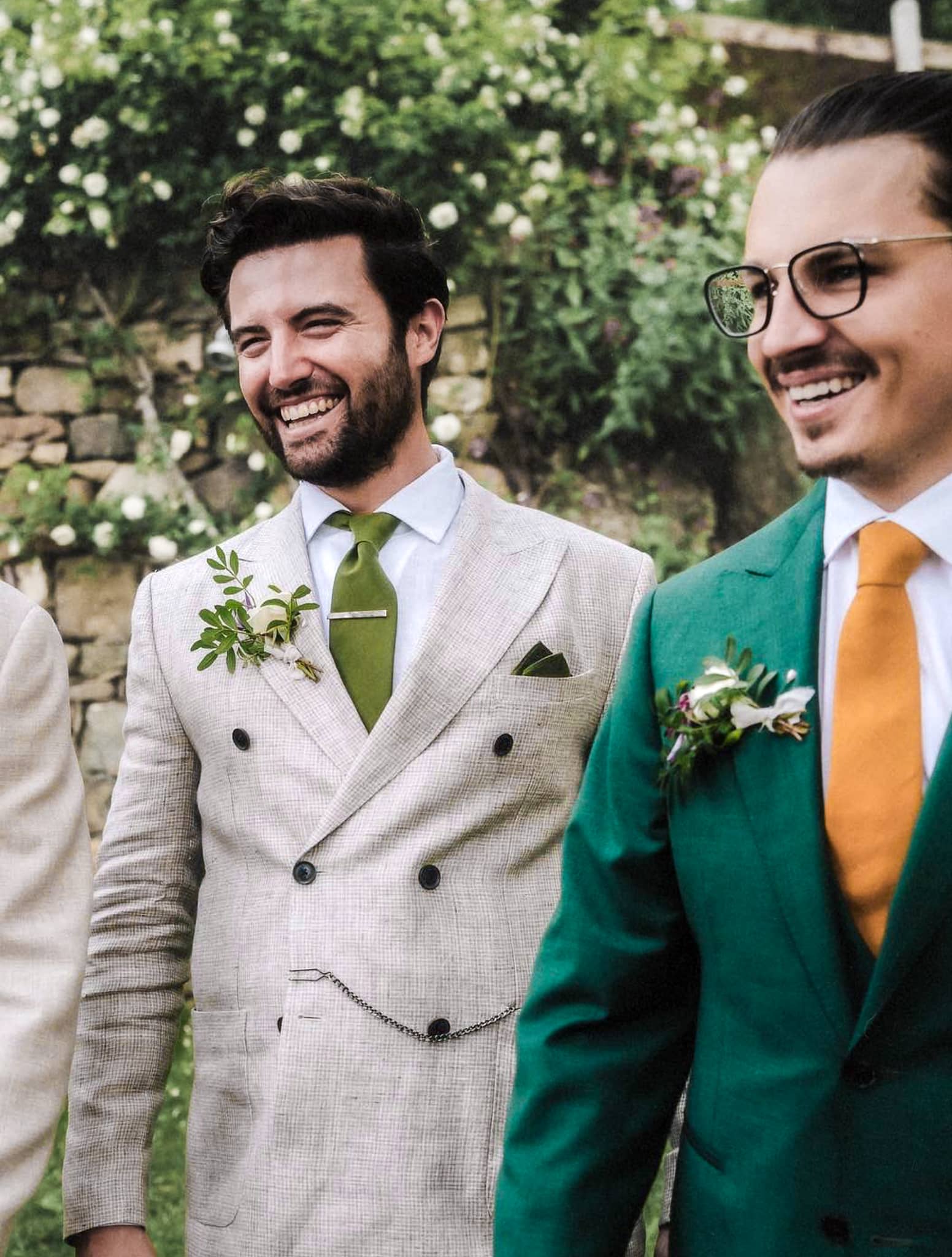 Groom and best man standing side by side. Groom wearing green solid Loro Piana custom wedding suit with white shirt and yellow tie. Best man in off white linen custom wedding suit and solid green tie.