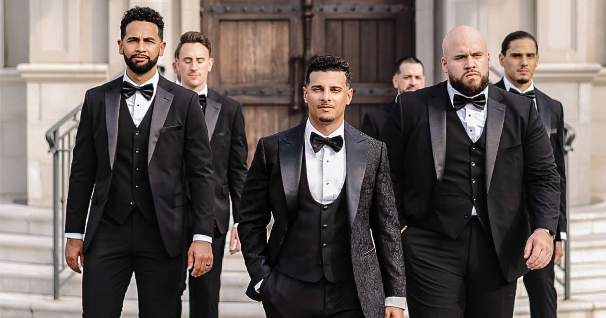 Groom and his five groomsmen standing outside church. All wearing vested custom tuxedos.