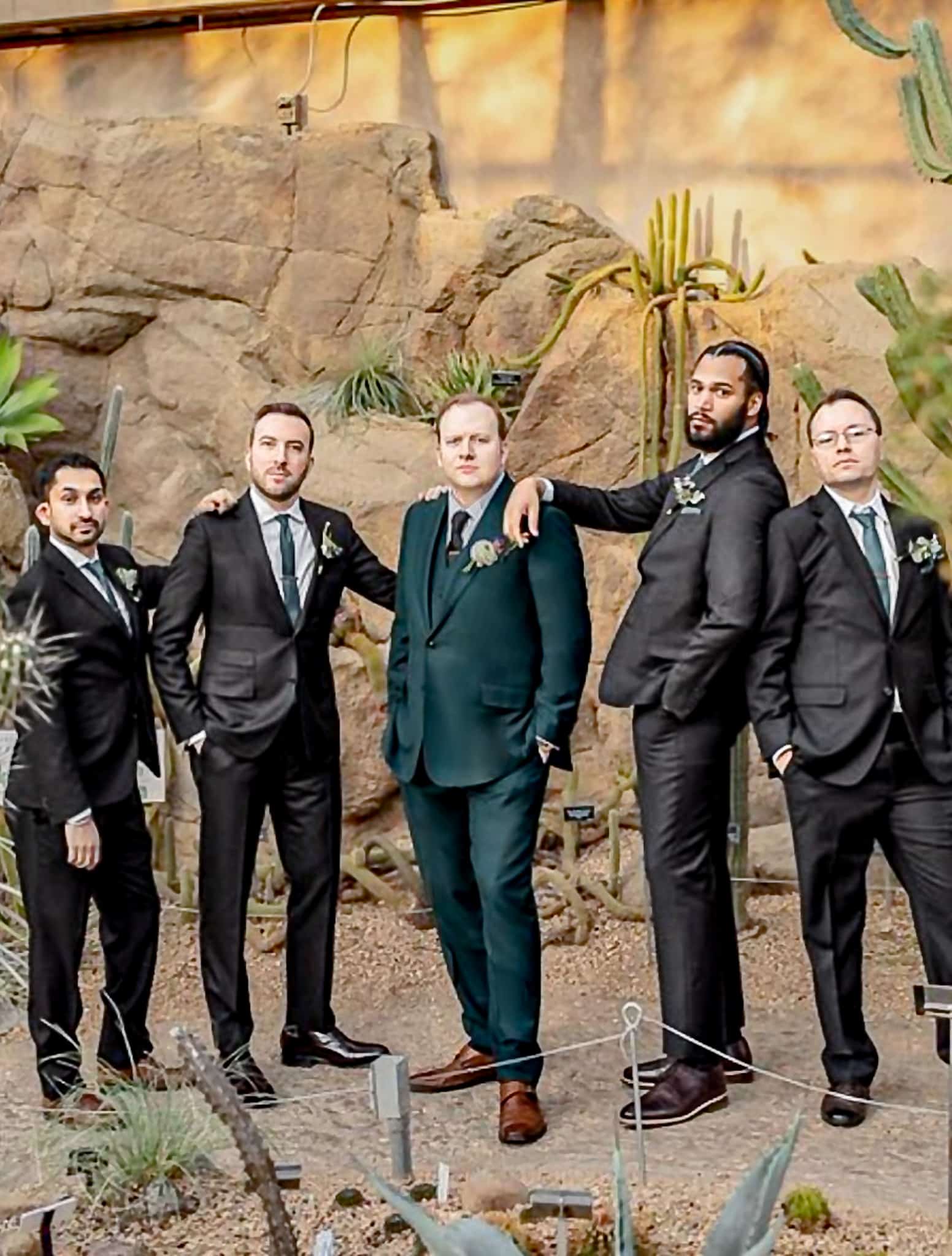 Five groomsmen standing side by side all in black wedding suits.