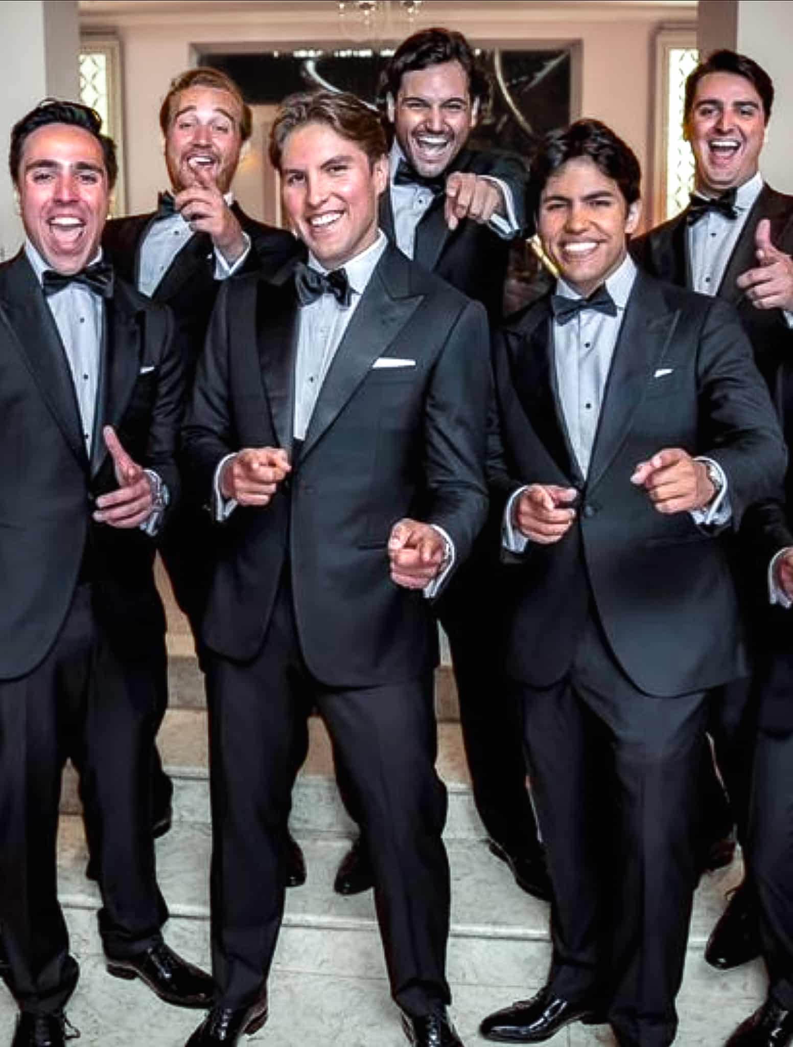 Six groomsmen all pointing and gesturing toward camera-all wearing custom wedding tuxedos.