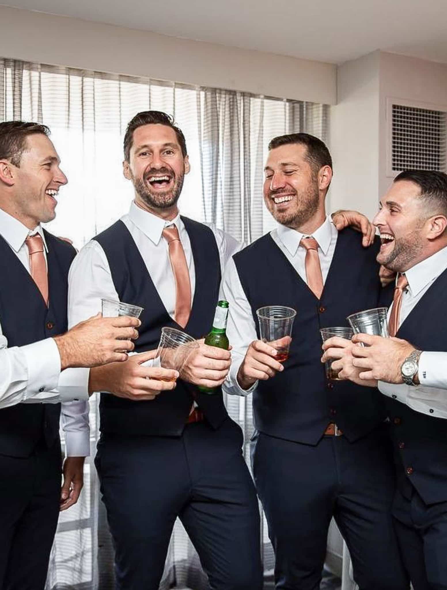 Four groomsmen all in matching navy vests and matching orange ties.