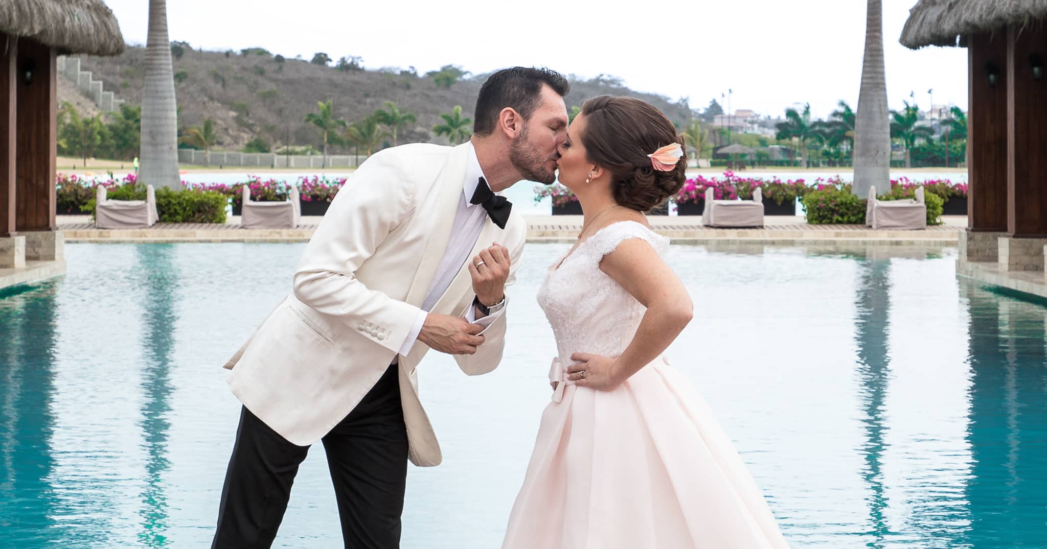 Bride and groom kissing while overlooking outdoor pool. Groom in custom Zegna white dinner jacket with black bowtie.