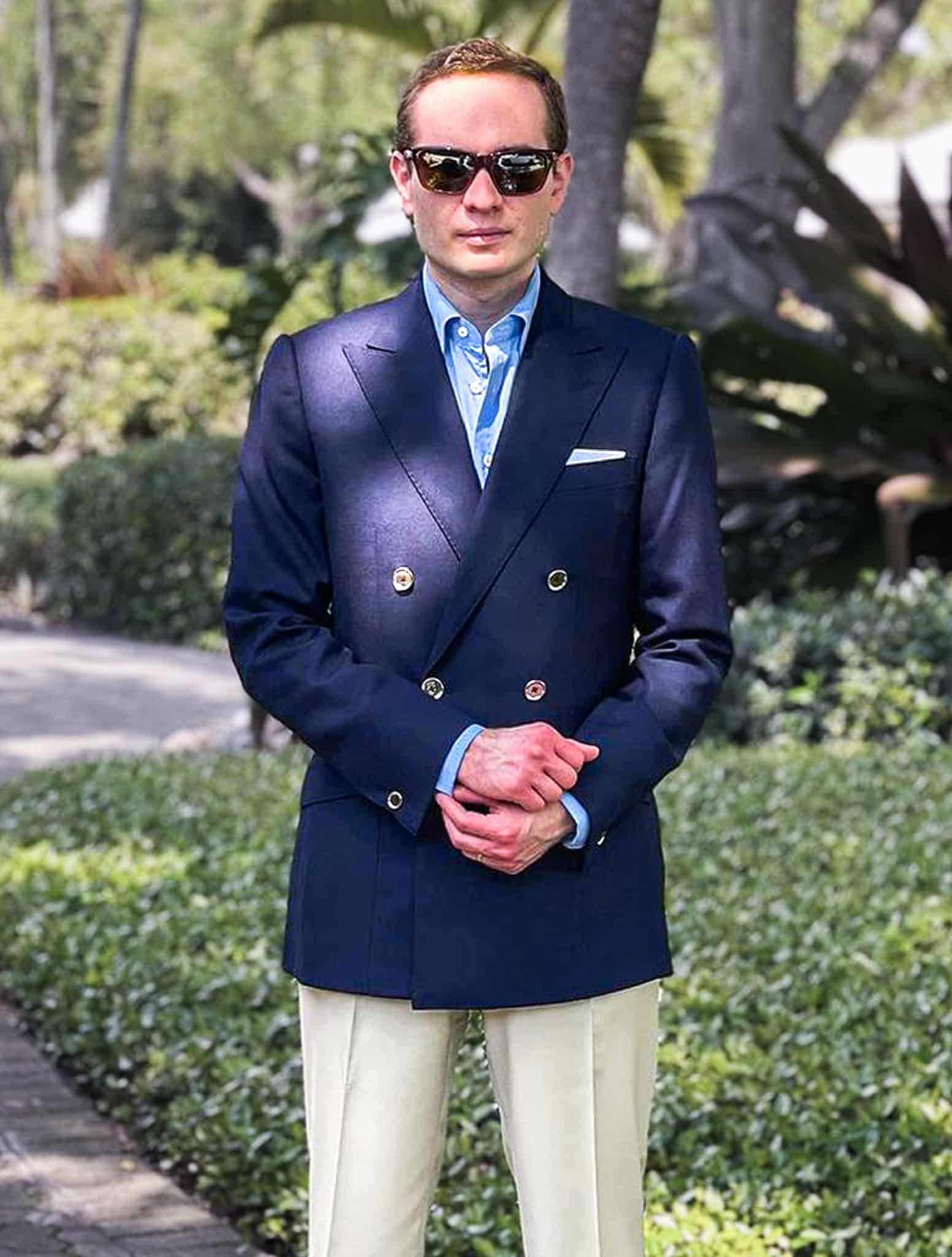 Groom outdoors wearing Piacenza navy blue double breasted custom blazer with white trousers and a light blue open collared shirt.