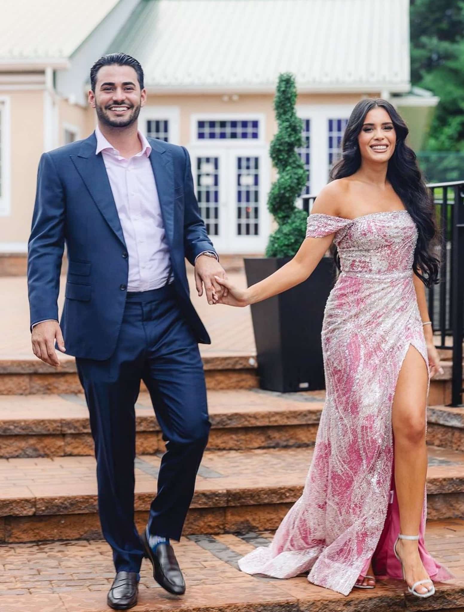 Groomsman and bridesmaid holding hands. Groomsman wearing blue bespoke wedding suit with light blue open collared dress shirt.
